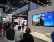 Un écran géant installé dans un salon professionnel, avec des visiteurs regardant une vidéo de présentation sur un stand moderne.
